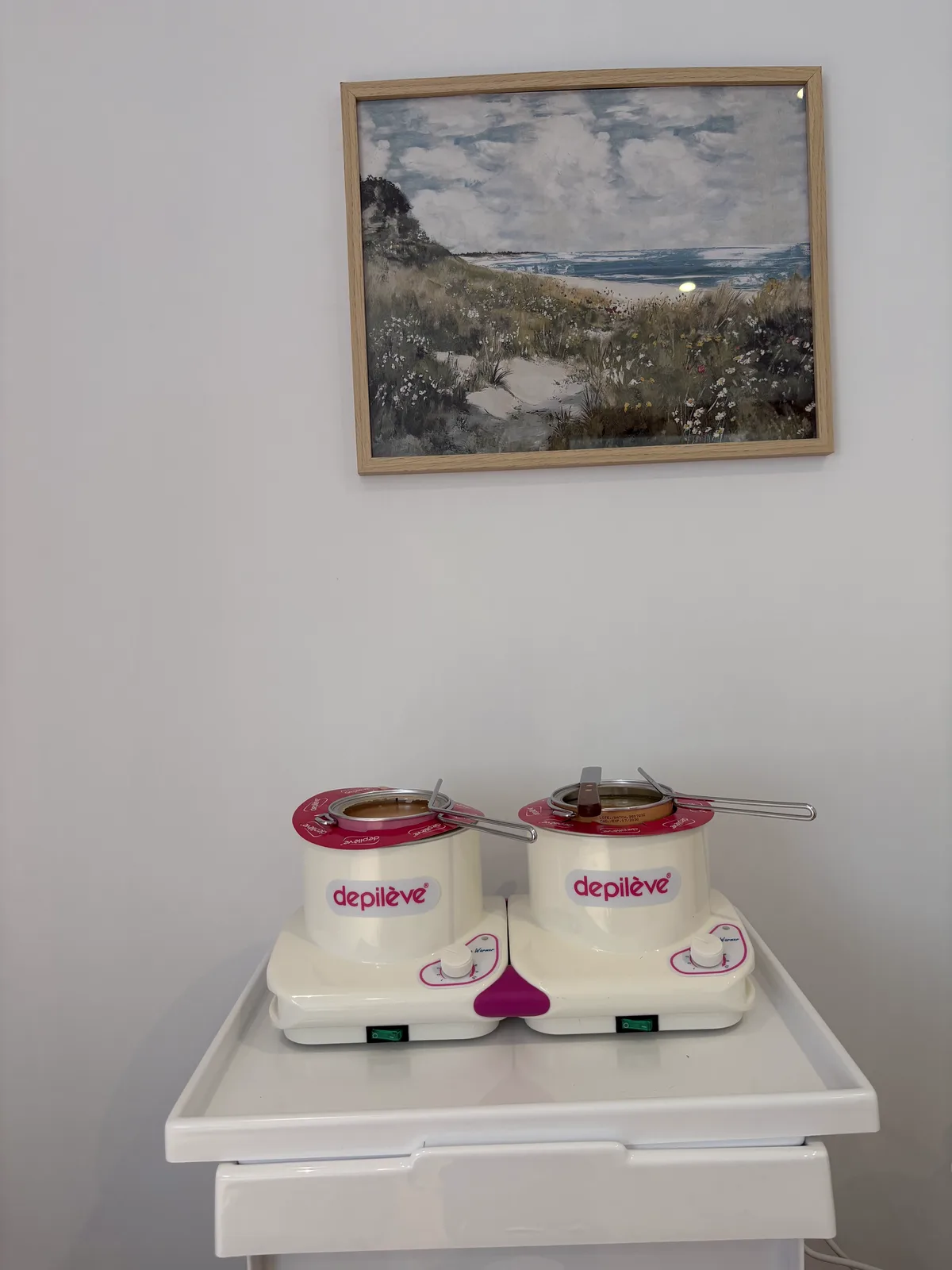 Deux chauffe-cires Dépilève posés sur un chariot blanc du studio, sous un tableau de bord de mer